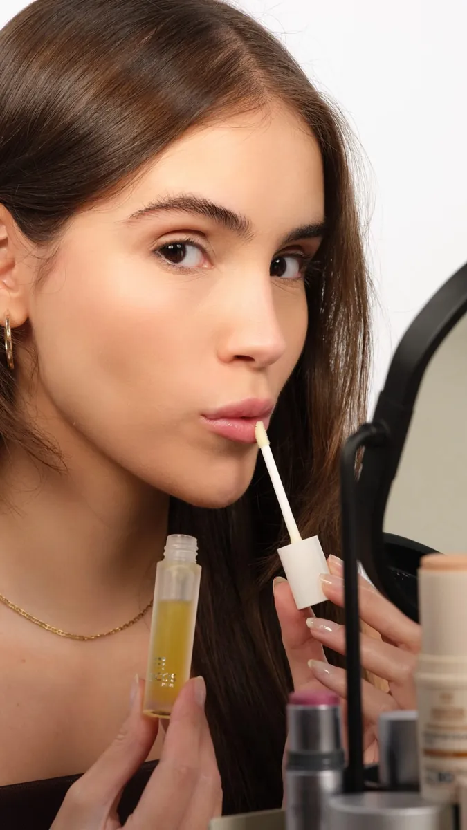 Beatriz aplicando um gloss diante do espelho
